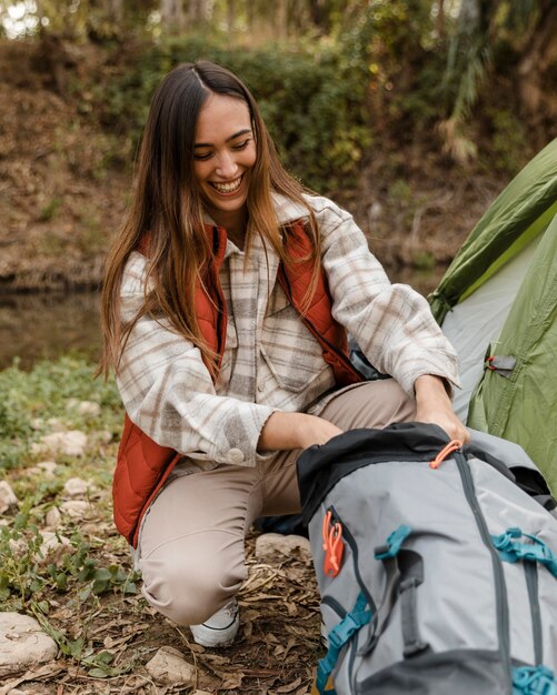 Garota feliz acampando na floresta olhando para a mochila