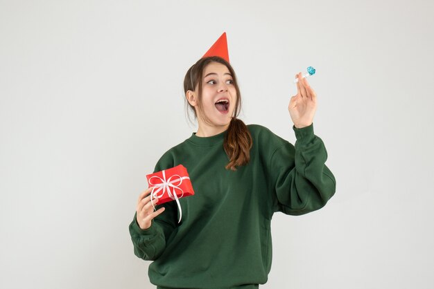 Garota feliz com boné de festa segurando seu presente de natal e fazendo barulho em branco