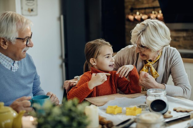 Garota feliz comendo biscoitos enquanto conversa com os avós na cozinha