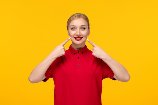 Garota feliz do dia da camisa vermelha apontando para a boca em uma camisa vermelha em um fundo amarelo