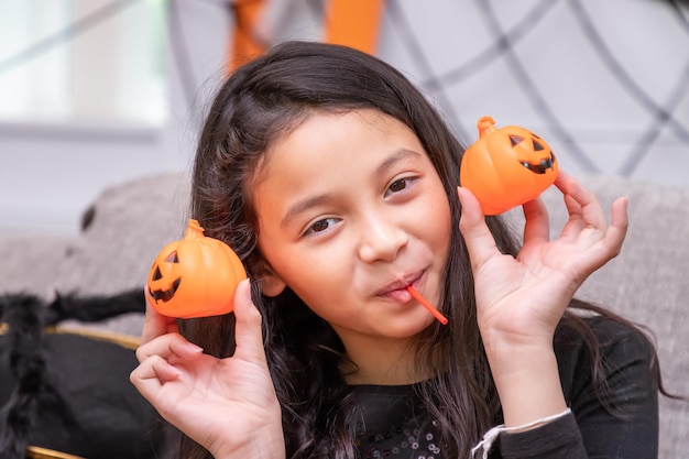 Garota feliz e fofa fantasiada durante a festa de Halloween segurando abóbora Jacko'lantern ao lado de seus olhos