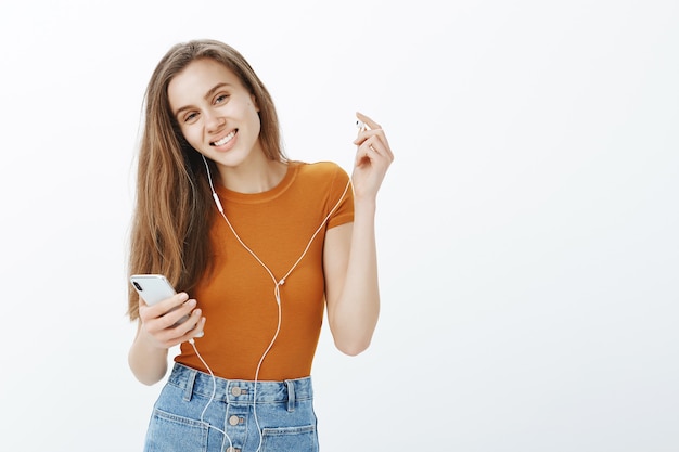 Garota feliz e sorridente tirando o fone de ouvido e olhando, ouvir podcast ou música no celular