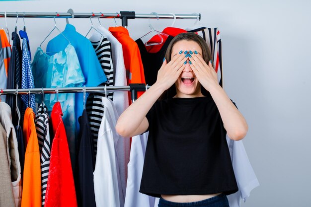 Garota feliz está cobrindo os olhos com as mãos no fundo da roupa