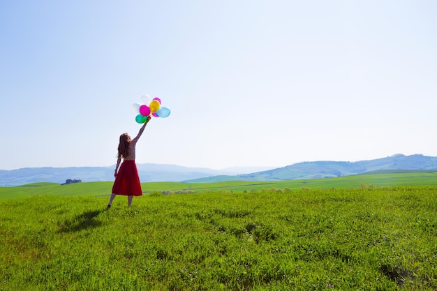 Garota feliz na toscana prados com balões coloridos, contra o céu azul e prado verde. toscana, itália