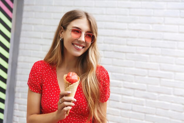 Garota feliz tomando sorvete em uma caminhada ao ar livre pela cidade, sorrindo, apreciando a doce comida de rua