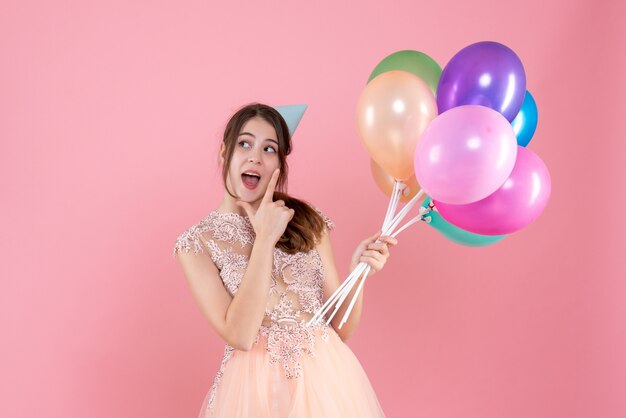 garota festeira feliz com boné segurando balões rosa