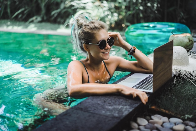 Garota freelancer trabalhando de férias. Jovem mulher com laptop trabalha enquanto está sentado em uma espreguiçadeira. Trabalhe de qualquer lugar, freelance.