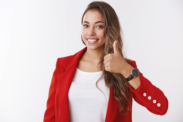 Garota garantindo que você tenha um dia de sorte. Feliz sorridente linda empresária mostrando o polegar, gostando de aprovar uma ideia incrível, deliciada em dar uma resposta positiva, concordo, parede branca de pé