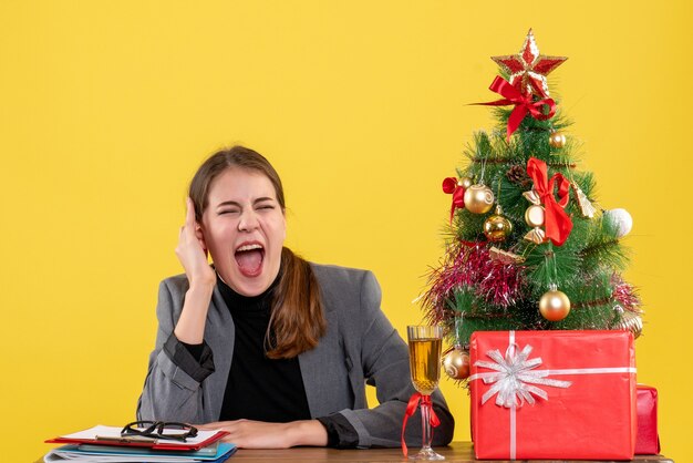 Garota gritada de vista frontal sentada na mesa árvore de natal e coquetel