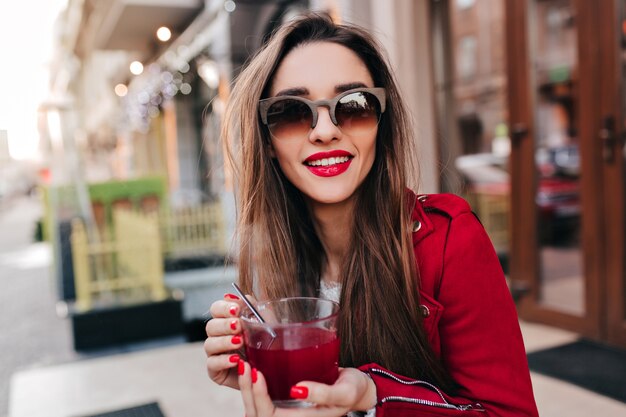 Garota incrível em óculos de sol castanhos bebendo chá com um sorriso