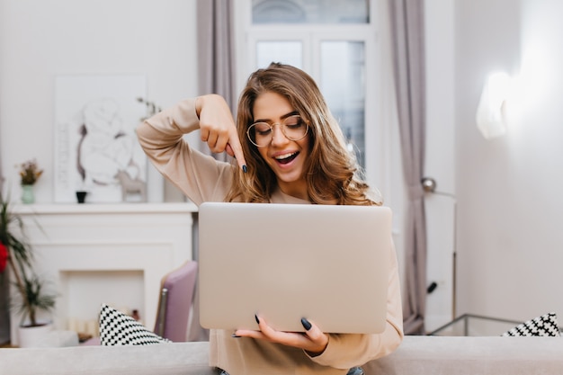 Foto grátis garota interessada com manicure da moda brincando em casa durante a sessão de fotos com laptop