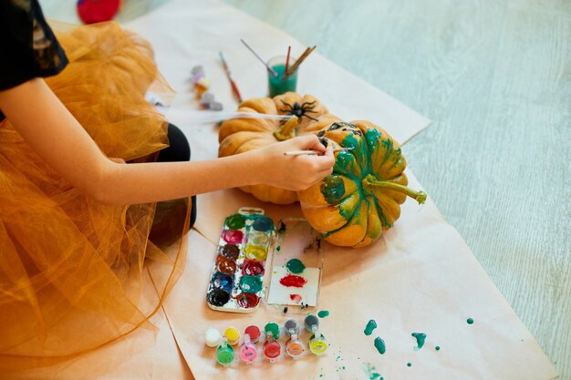 Garota irreconhecível decorando uma abóbora laranja, desenhando o rosto de jack-o-lantern para o halloween