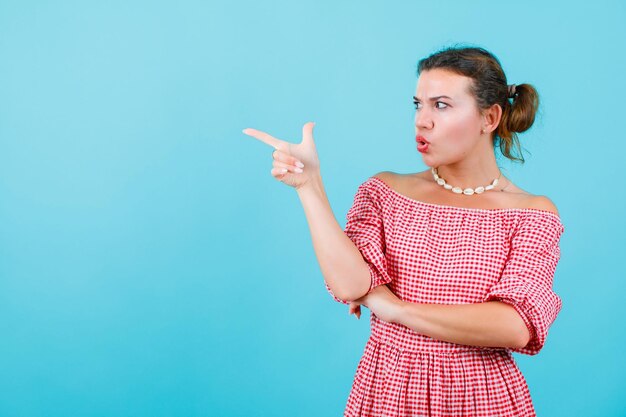 Garota irritada está olhando e apontando para a direita com o dedo indicador sobre fundo azul