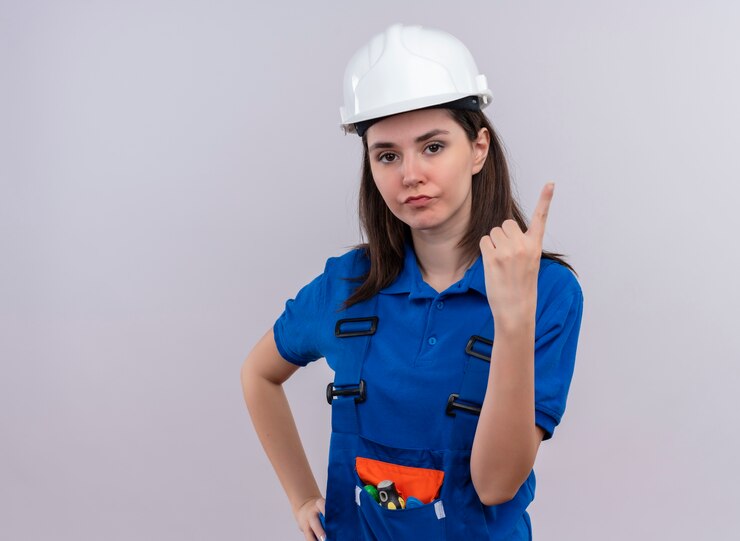 Foto grátis garota jovem construtora irritada com capacete de segurança branco e uniforme azul aponta para cima em um fundo branco isolado com espaço de cópia