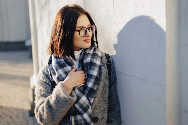 Garota jovem e atraente de óculos em um casaco andando em um dia ensolarado