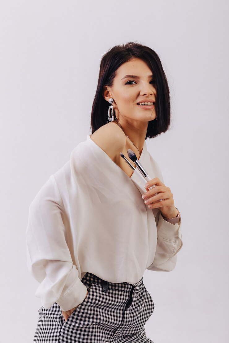 Garota jovem e atraente negócios com pincéis de maquiagem posando no fundo liso. conceito de maquiagem e cosméticos.