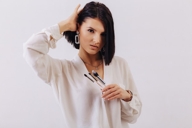 Garota jovem e atraente negócios com pincéis de maquiagem posando no fundo liso. conceito de maquiagem e cosméticos.