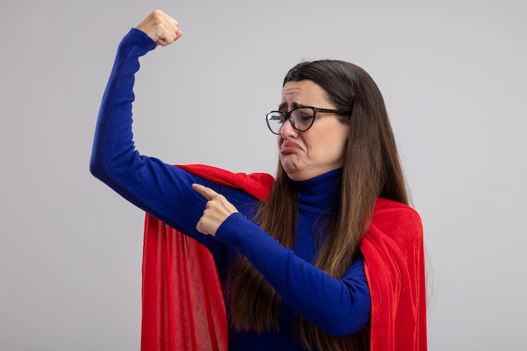 Foto grátis garota jovem e triste super-heroína usando óculos, mostrando um gesto forte, isolado no fundo branco