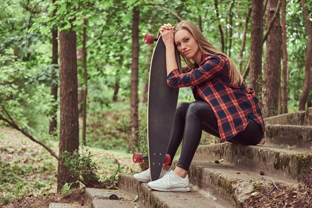 Garota jovem hipster loira descansando em um parque, depois de andar de skate.
