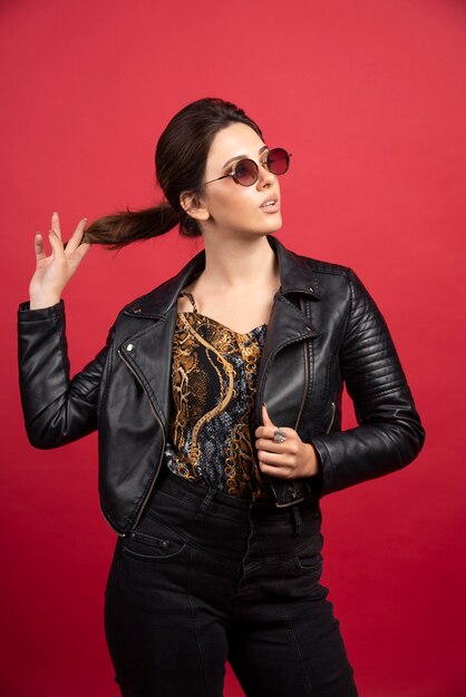 Garota legal em uma jaqueta de couro preta e óculos escuros parece severa e exigente.