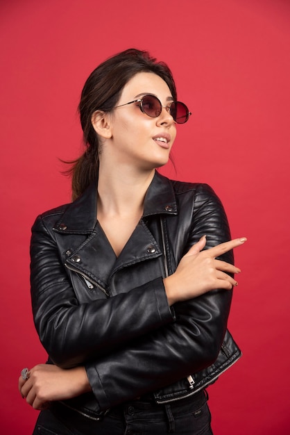 Garota legal na jaqueta de couro preta, posando de óculos de sol pretos.