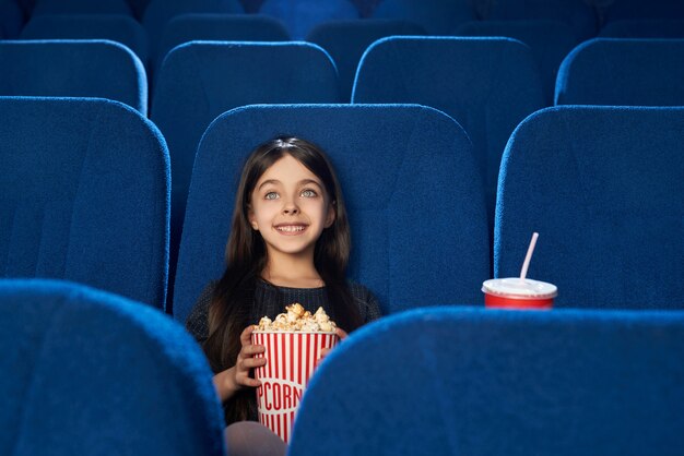 Garota linda e feliz assistindo filme com pipoca no cinema.