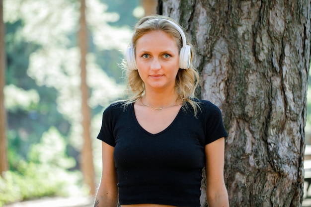 Garota loira com fone de ouvido está olhando para a câmera no fundo da natureza