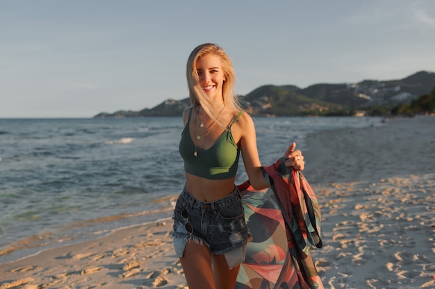 Garota loira feliz correndo na praia, aproveitando o verão.