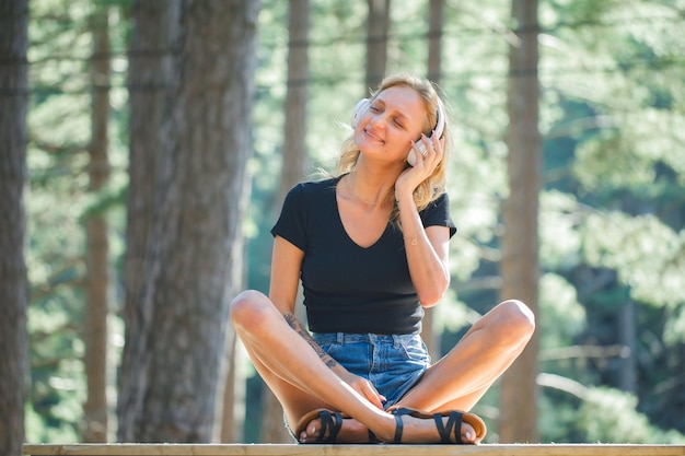 Garota loira feliz está desejando enquanto ouve música no fone de ouvido no fundo da natureza