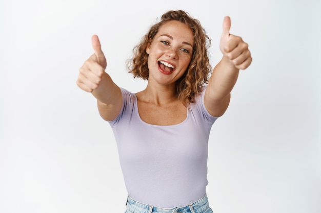 Foto grátis garota loira feliz mostra os polegares para cima e sorrindo, elogia, elogia, recomenda um bom produto ou serviço em branco.