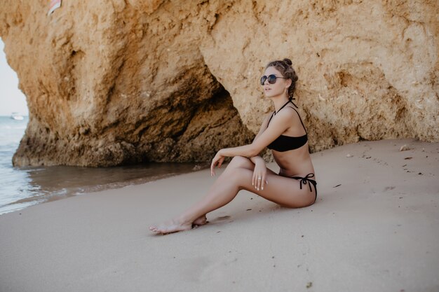 Garota loira sexy de biquíni preto posando em uma praia