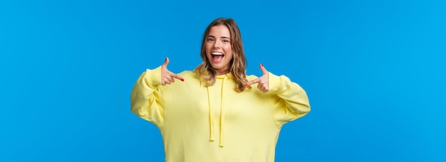 Foto grátis garota loira sorridente e confiante com capuz amarelo apontando para si mesma sugere a própria ajuda w