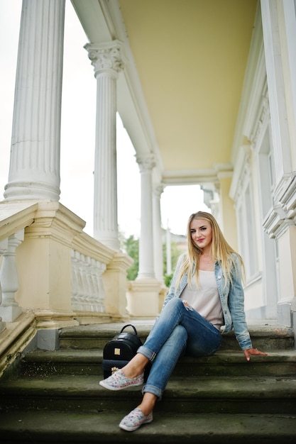 Garota loira usa jeans com mochila posada contra casa vintage