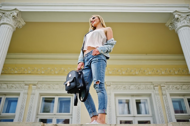 Foto grátis garota loira usa jeans com mochila posada contra casa vintage