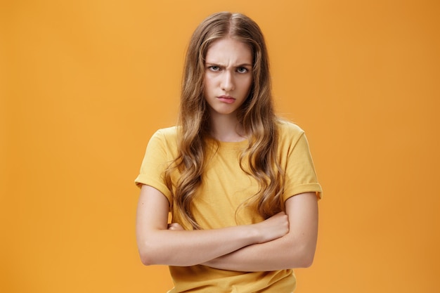 Garota louca como o diabo. retrato de uma jovem odiosa com raiva, incomodada e ofendida, olhando por baixo da testa, franzindo a testa e amuando, cruzando os braços contra o peito em pose defensiva, desprezando o ofensor.