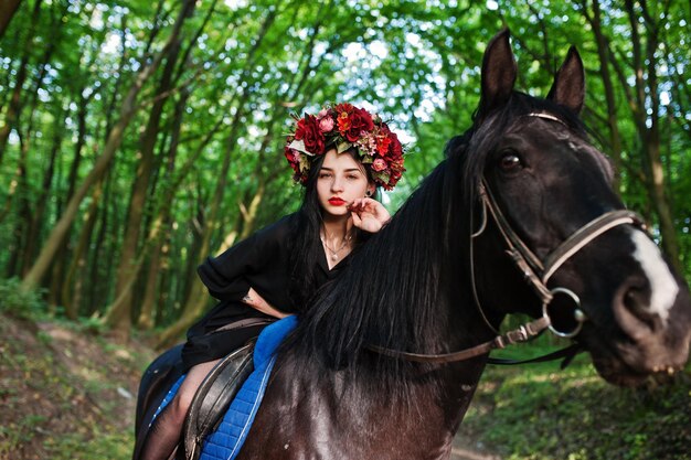Garota mística em grinalda veste de preto a cavalo em madeira