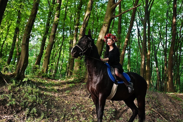 Garota mística em grinalda veste de preto a cavalo em madeira