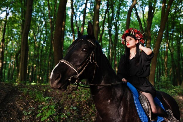 Garota mística em grinalda veste de preto a cavalo em madeira