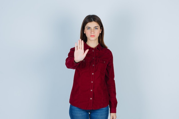 garota mostrando gesto de parada na camisa cor de vinho e parecendo decidida.