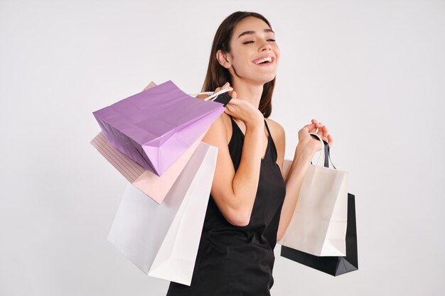 Garota muito alegre segurando sacolas de compras olhando alegremente na câmera sobre fundo branco