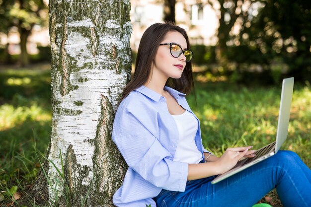 Garota muito séria de jeans trabalha com laptop no parque da cidade
