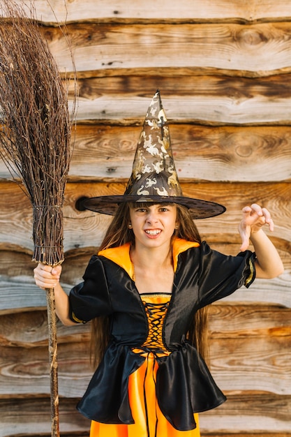 Garota na fantasia de bruxa mostrando chegar a mão com cabo de vassoura