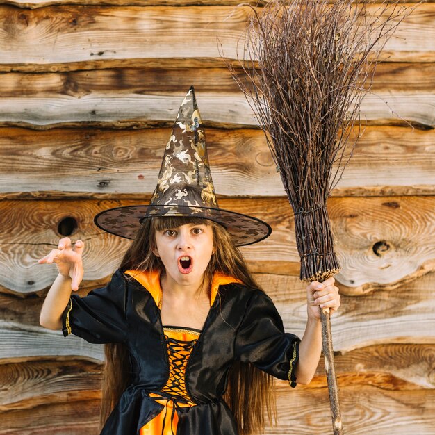 Garota na fantasia de bruxa mostrando horror com cabo de vassoura