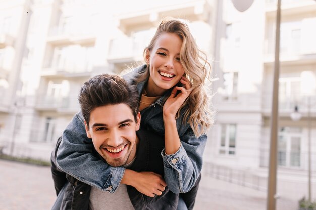 garota na jaqueta jeans, abraçando o namorado. Casal caucasiano sorridente posando juntos na rua.