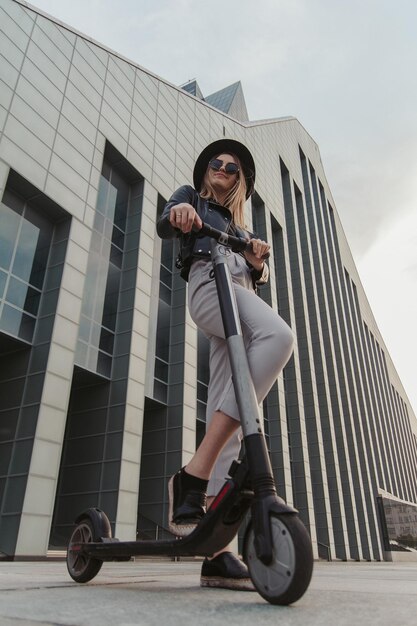 Garota na moda atraente em óculos de sol e chapéu está posando para o fotógrafo com sua nova scooter.