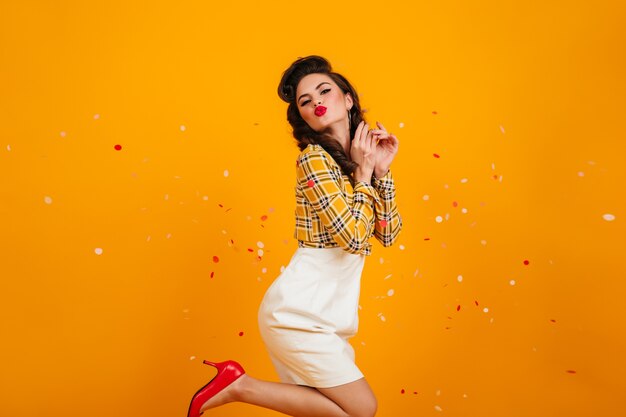 Garota Pin-up romântica dançando sobre fundo amarelo. Foto de estúdio de uma jovem brincalhona de saia branca.