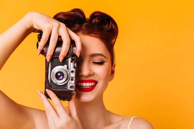 Garota pinup feliz tirando fotos. Retrato de estúdio de mulher com câmera isolada no espaço amarelo.