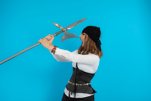 Garota pirata jovem com raiva segurando uma lança e gritando sobre um fundo azul. Foto de alta qualidade