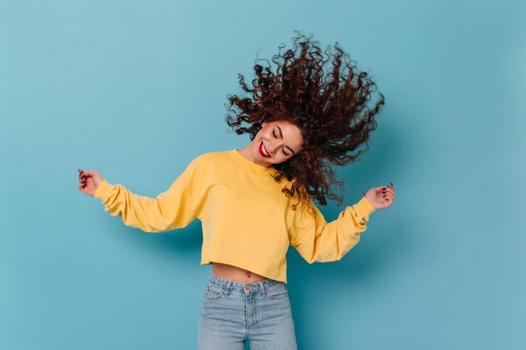 Foto grátis garota positiva em moletom brilhante toca cabelo ri e dança em fundo azul isolado