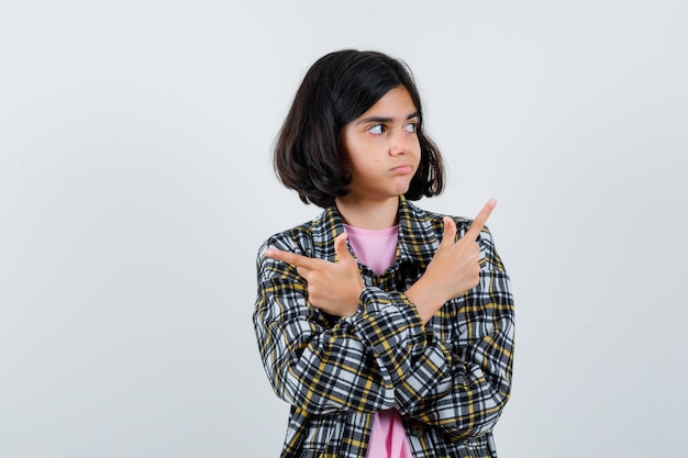 Garota pré-adolescente apontando para lados diferentes na camisa, jaqueta, vista frontal.